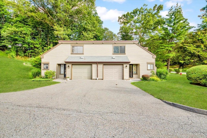 View of front of home featuring asphalt driveway, an attached garage, a front lawn, view of scattered trees, and roof with shingles