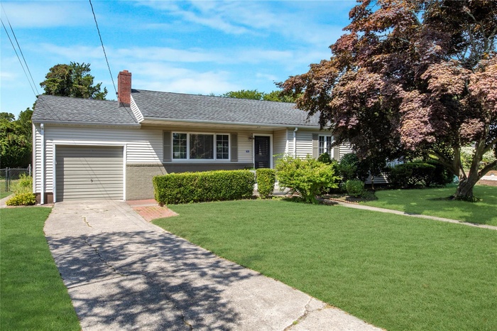 Ranch-style house featuring an attached garage, a chimney, driveway, roof with shingles, and brick siding
