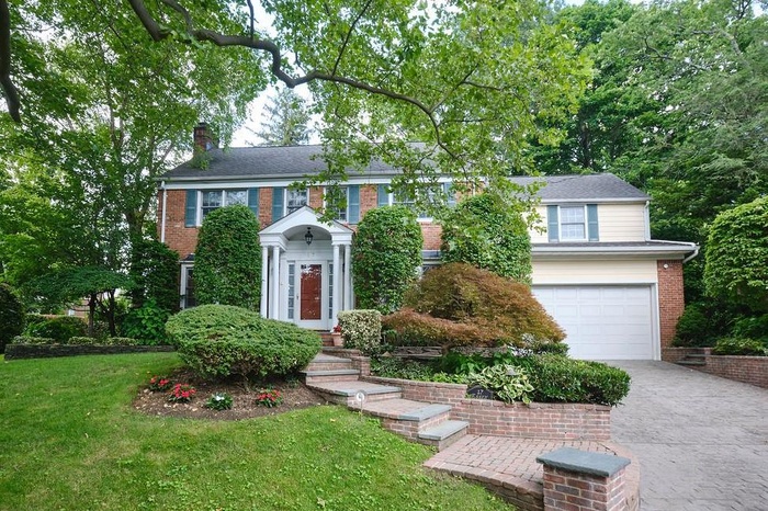 Colonial home featuring driveway, a chimney, an attached garage, brick siding, and a front yard