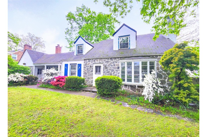 Cape cod house featuring stone siding, a front lawn, a chimney,
