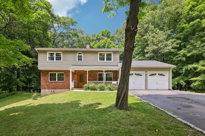 View of front of home featuring a garage, a porch, driveway, a front lawn, and brick siding