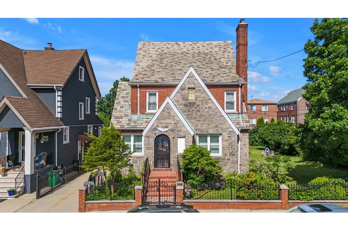 English style home with a high end roof, a fenced front yard, a chimney, a gate, and stone siding