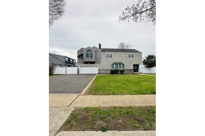View of front of home featuring fence, a front lawn, an attached garage, a chimney, and driveway