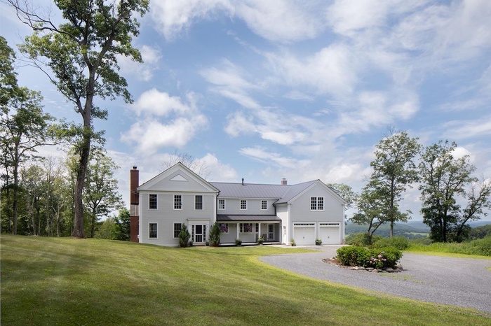 View of front of house with a chimney, an attached garage, gravel driveway, and a front lawn