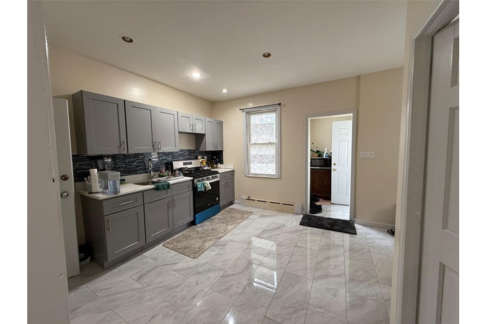 Kitchen featuring gray cabinets, gas range, baseboard heating, decorative backsplash, and light countertops