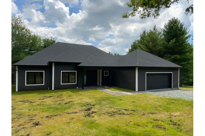 Ranch-style house with an attached garage, roof with shingles, and a front yard