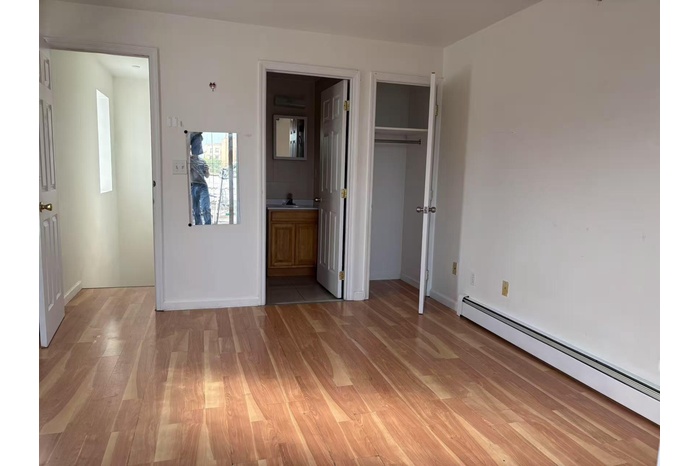 Unfurnished bedroom featuring light wood-style flooring, a baseboard heating unit, ensuite bathroom, and a closet