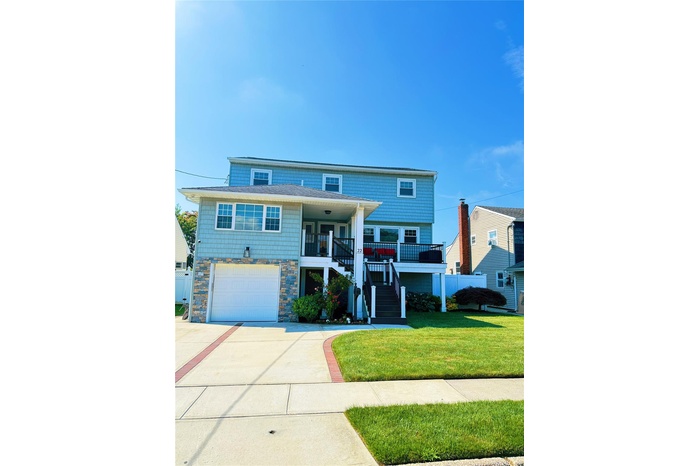 View of front of house with stairway, driveway, a front lawn, an attached garage, and covered porch