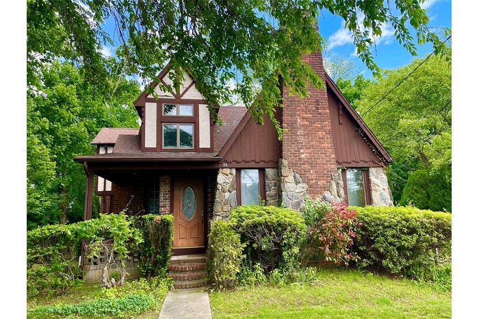 Tudor home with a chimney, stone siding, and roof with shingles