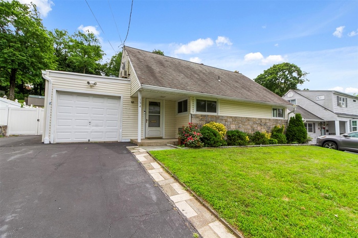 View of front of property featuring an attached garage, stone siding, driveway, and a shingled roof