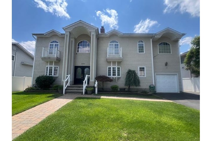 View of front of house featuring driveway, a garage, a chimney, a balcony, and french doors