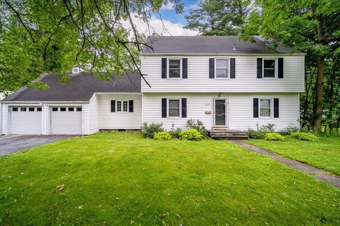 Colonial inspired home featuring asphalt driveway, an attached garage, a front yard, and roof with shingles