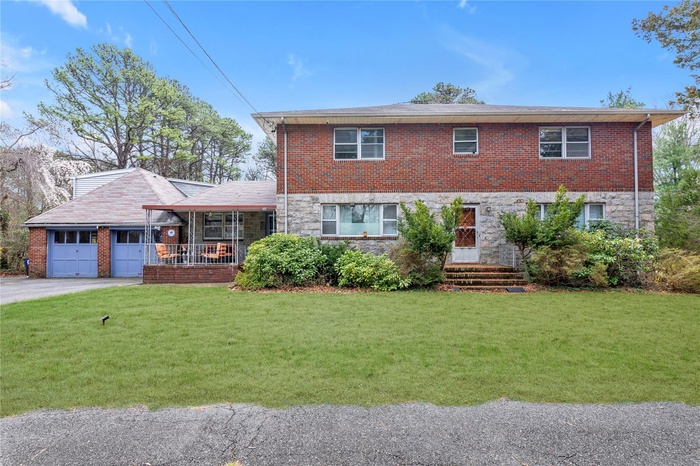 View of front facade with a garage, a porch, stone siding, and a front yard