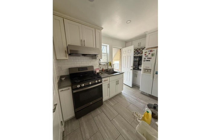 Kitchen featuring stainless steel gas range oven, white fridge with ice dispenser, under cabinet range hood, dark countertops, and decorative backspla