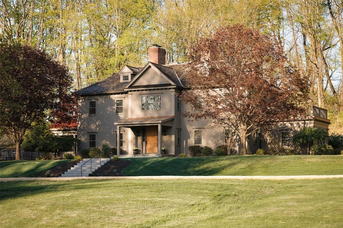 Shingle-style home featuring a front lawn, a chimney, and a standing seam roof