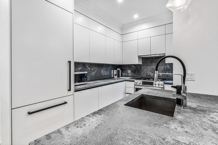 Kitchen featuring sink, white cabinetry, tasteful backsplash, ornamental molding, and dark stone counters