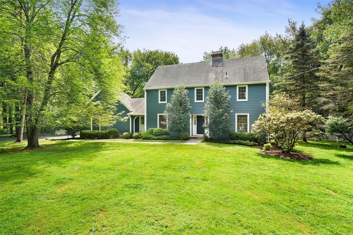 Colonial home featuring a front lawn, a chimney, and view of wooded area