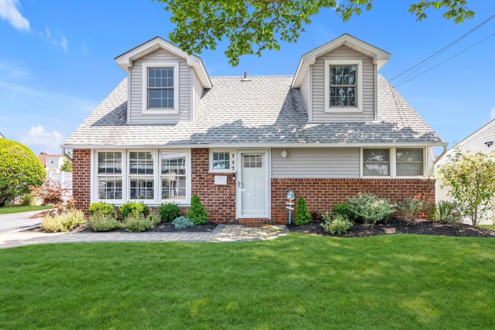 Cape cod house with brick siding, a front yard, and a shingled roof