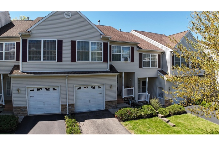 Townhome / multi-family property with an attached garage, roof with shingles, stone siding, and asphalt driveway