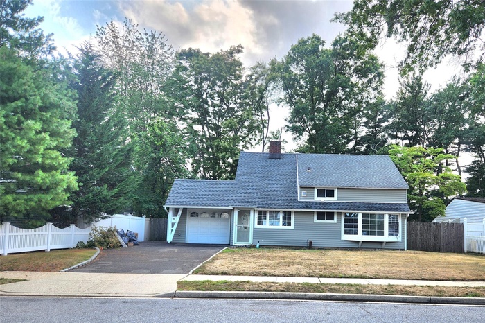 View of front of property with asphalt driveway, a garage, a chimney, and view of scattered trees