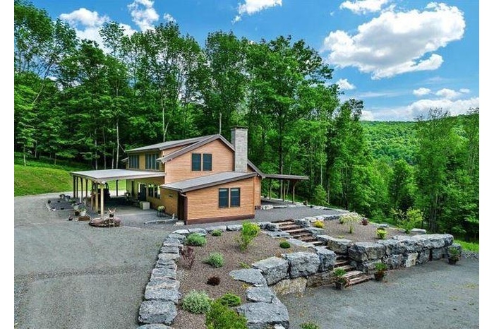 View of side of home with a chimney, a forest view, and a porch