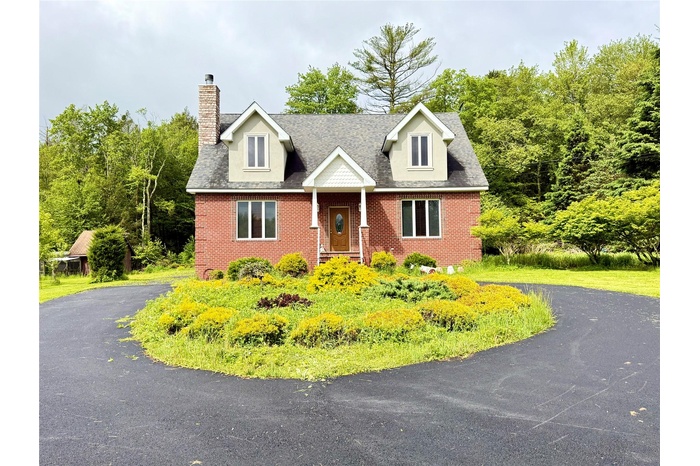 New england style home featuring a chimney, brick siding, and asphalt driveway