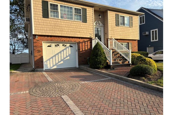 Raised ranch featuring brick siding, an attached garage, and decorative driveway