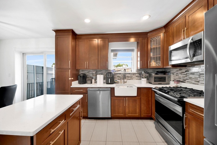 Kitchen with stainless steel appliances, backsplash, light tile patterned flooring, light countertops, and glass insert cabinets