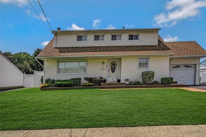 View of front facade featuring a garage, a shingled roof, driveway, and a chimney
