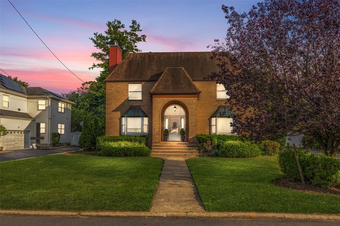 View of front of property with a chimney, a front yard, brick siding, and a shingled roof