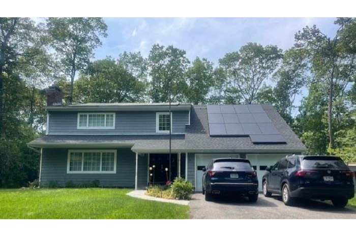 Traditional home with roof mounted solar panels, a garage, a chimney, a front lawn, and driveway