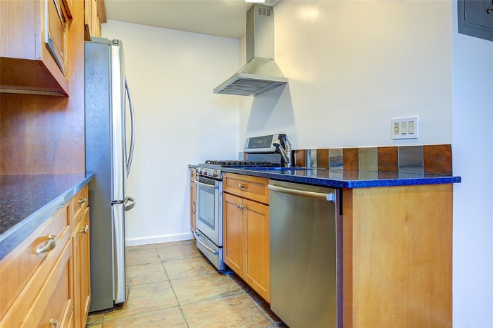 Kitchen with ventilation hood, appliances with stainless steel finishes, light tile patterned floors, and dark stone counters