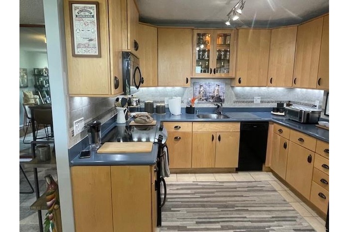 Kitchen featuring tasteful backsplash, dark countertops, black appliances, glass insert cabinets, and light tile patterned flooring