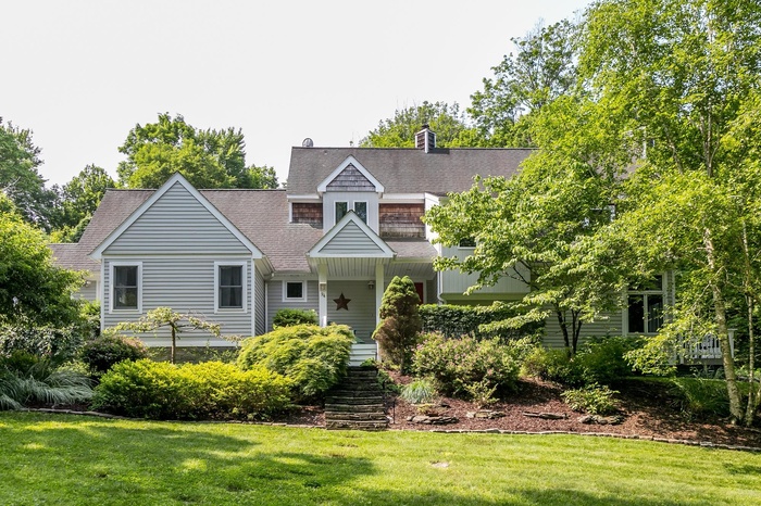View of front facade featuring a front yard, roof with shingles, stairs, and a chimney