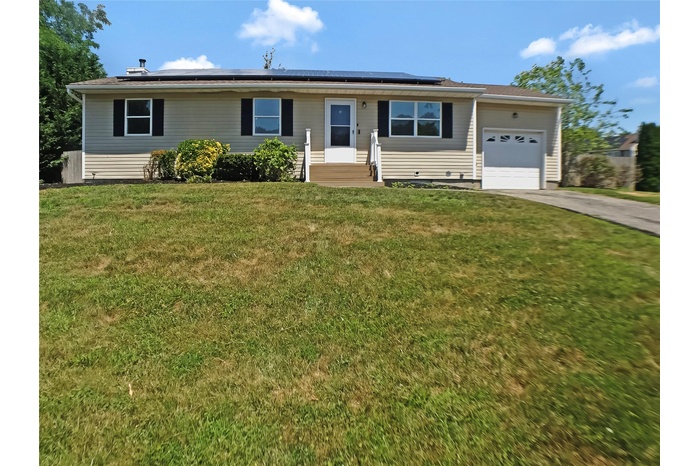 Ranch-style home featuring a garage, driveway, roof mounted solar panels, and a front yard