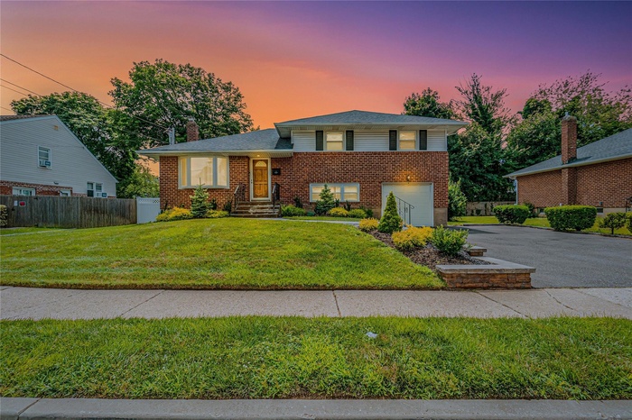 Tri-level home featuring asphalt driveway, brick siding, a chimney, and an attached garage