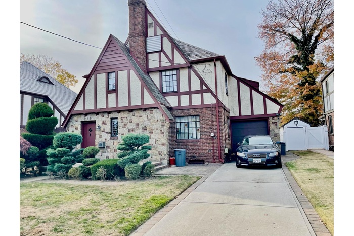 Tudor home with a gate, stucco siding, concrete driveway, a chimney, and a garage