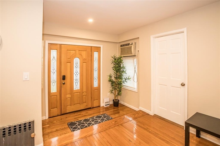 Entryway with radiator, light wood finished floors, and a wall unit AC