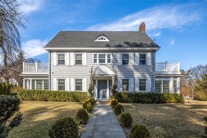 Colonial-style house with a balcony, a chimney, a front lawn, and roof with shingles