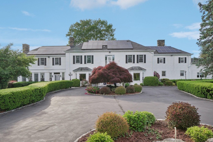 View of front of property with a chimney, curved driveway, and solar panels
