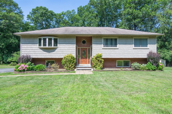 Raised ranch with a front lawn, brick siding, and roof with shingles