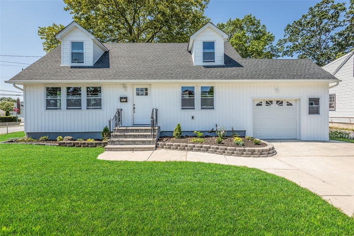 View of front facade featuring a shingled roof, an attached garage, a front lawn, and concrete driveway