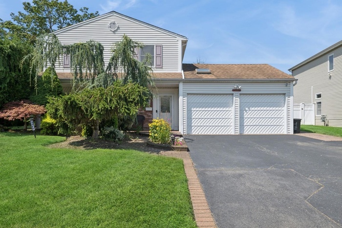 View of front facade with an attached garage, a front yard, driveway, and a shingled roof
