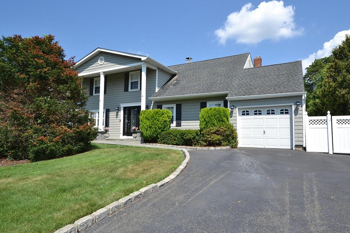 Neoclassical home with a shingled roof, a garage, driveway, and a chimney