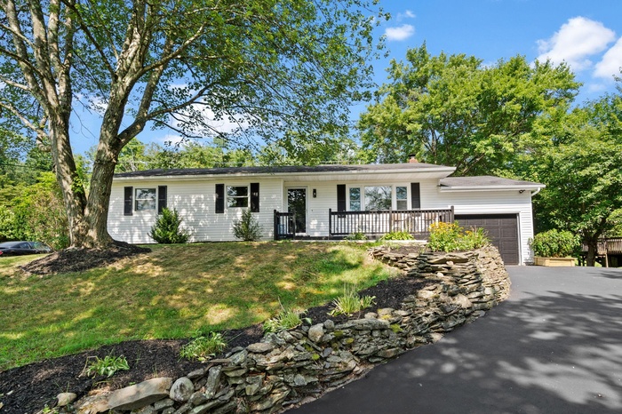 Ranch-style house with a garage, a porch, a chimney, a front yard, and asphalt driveway