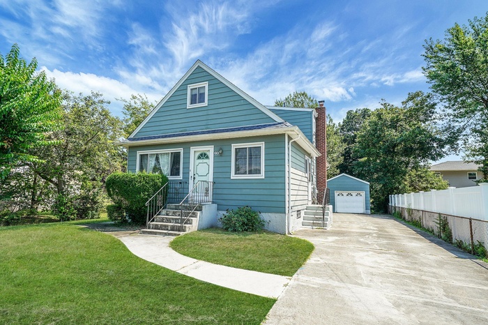 Bungalow-style home featuring a detached garage, a chimney, an outbuilding, and concrete driveway