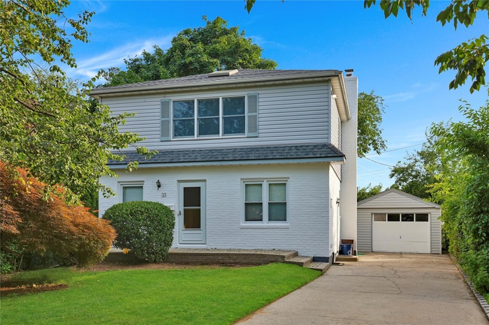 View of front of property with an outbuilding, a chimney, a shingled roof, a front lawn, and concrete driveway