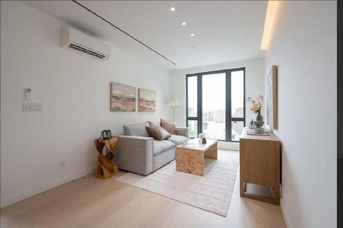 Living area with light wood-type flooring, a wall mounted air conditioner, and recessed lighting