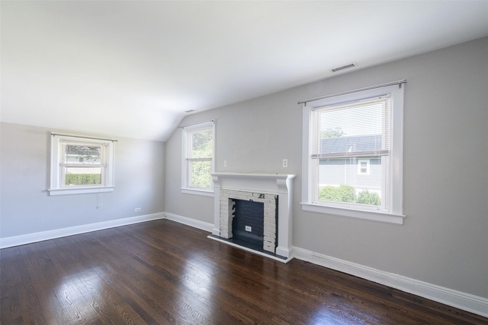 Unfurnished living room featuring plenty of natural light, vaulted ceiling, dark wood-style floors, and a fireplace