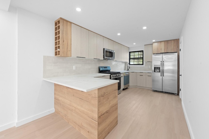 Kitchen with appliances with stainless steel finishes, light wood finished floors, decorative backsplash, a peninsula, and recessed lighting